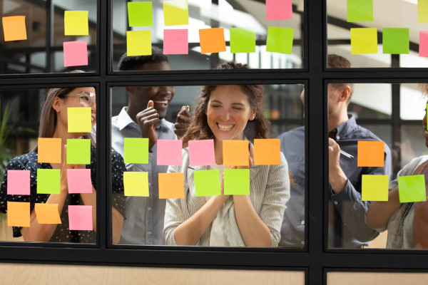 Excited multiracial work team finish task or project on post it stickers celebrate shared success in office, overjoyed multiethnic colleagues triumph complete group task, teamwork achievement concept