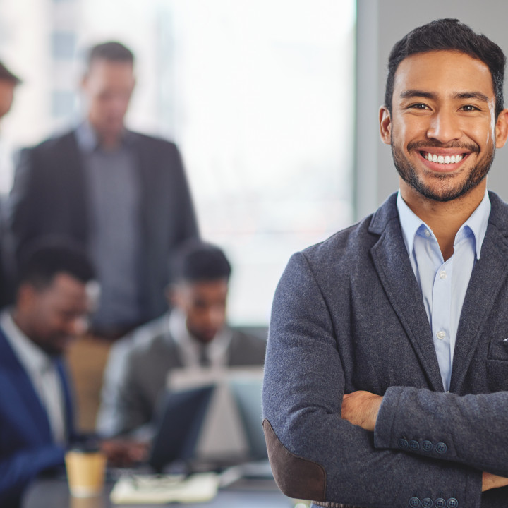 Portrait of a young businessman at the office standing in front of his colleagues having a meeting in the background.